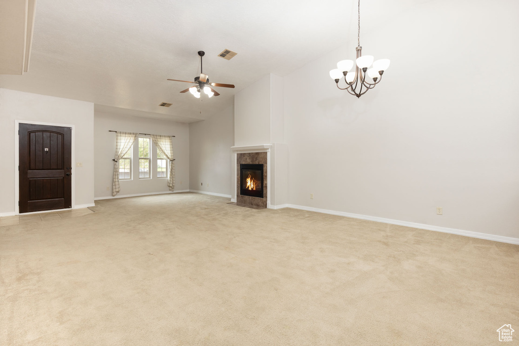 Unfurnished living room with a tile fireplace, ceiling fan with notable chandelier, light colored carpet, and vaulted ceiling