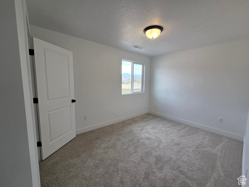Unfurnished room with a textured ceiling, carpet floors, baseboards, and visible vents