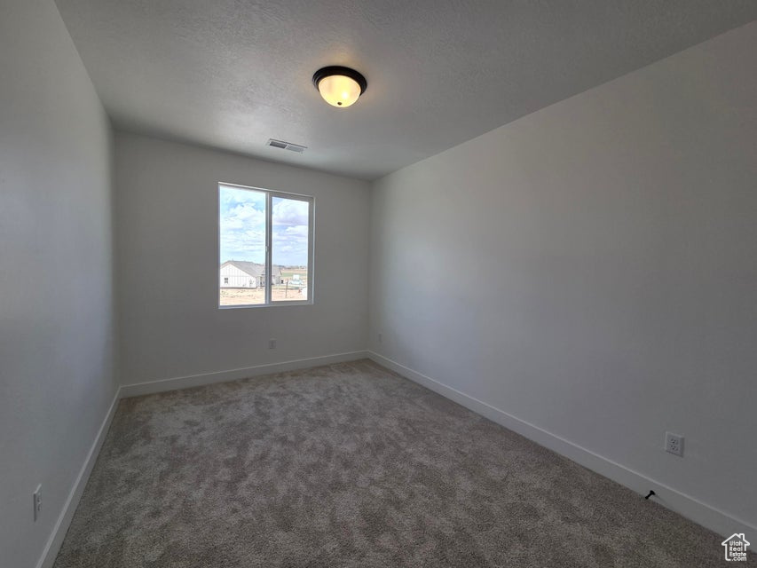 Carpeted spare room featuring a textured ceiling, baseboards, and visible vents