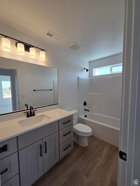 Bathroom with toilet, visible vents, vanity, wood finished floors, and bathing tub / shower combination