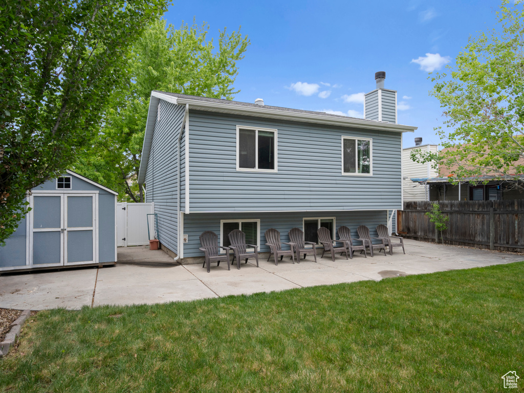 Rear view of property featuring a lawn, an outbuilding, a patio, a shed, and a fenced backyard
