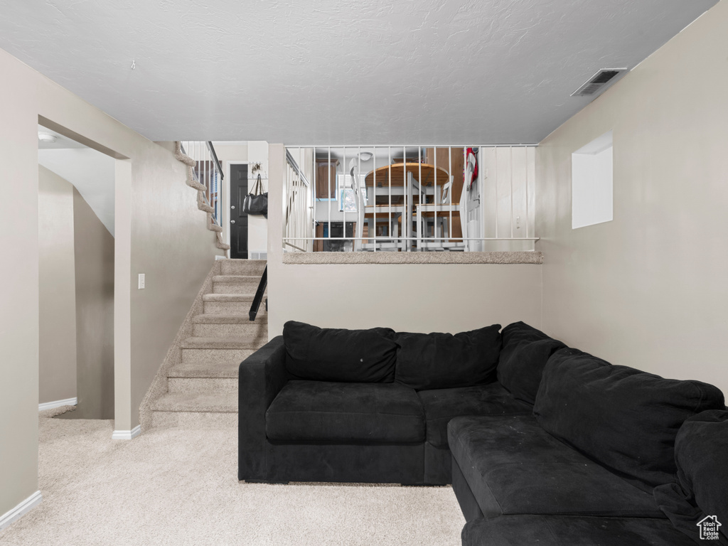 Carpeted living room with visible vents, baseboards, and stairway