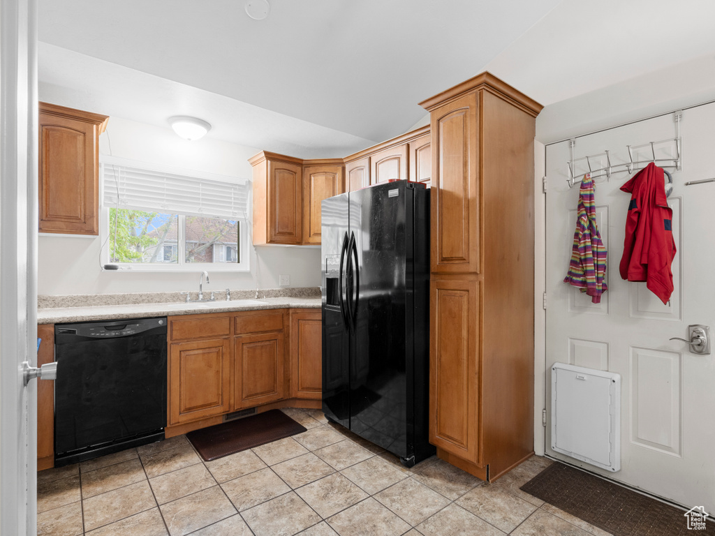 Kitchen featuring light countertops, light tile patterned floors, black appliances, and a sink