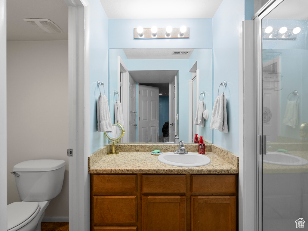 Bathroom with toilet, a shower with shower door, vanity, and visible vents
