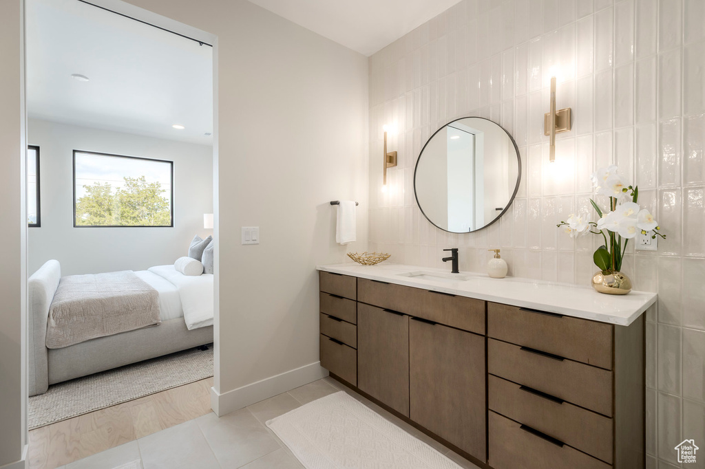 Ensuite bathroom with baseboards, tile patterned floors, vanity, connected bathroom, and backsplash