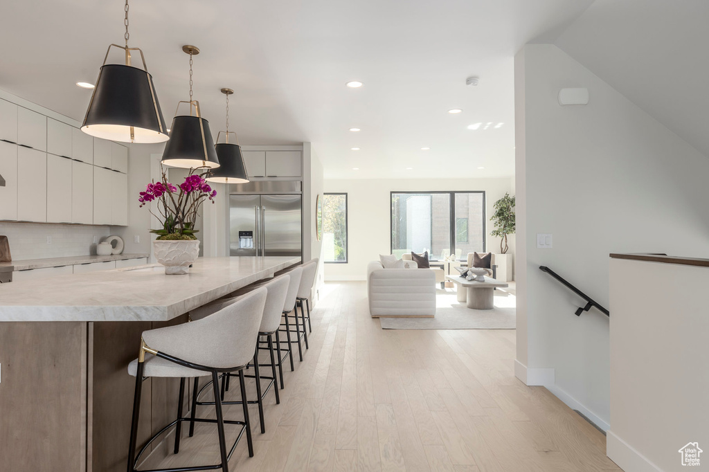 Kitchen with a breakfast bar, modern cabinets, stainless steel built in fridge, light wood-style floors, and light countertops
