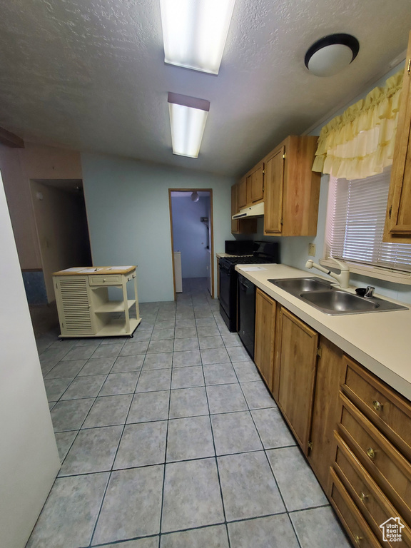 Kitchen featuring a sink, light countertops, black appliances, under cabinet range hood, and light tile patterned flooring