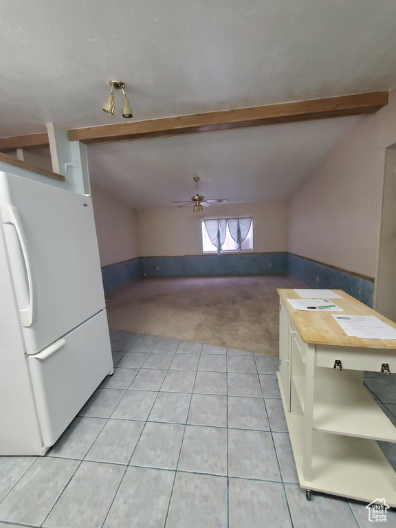 Interior space featuring light tile patterned flooring, a ceiling fan, light colored carpet, and vaulted ceiling with beams