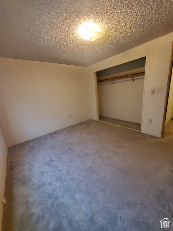 Unfurnished bedroom featuring carpet flooring, a textured ceiling, and a closet