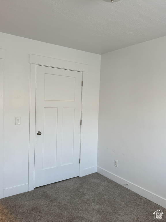 Unfurnished bedroom with a textured ceiling, dark colored carpet, and baseboards
