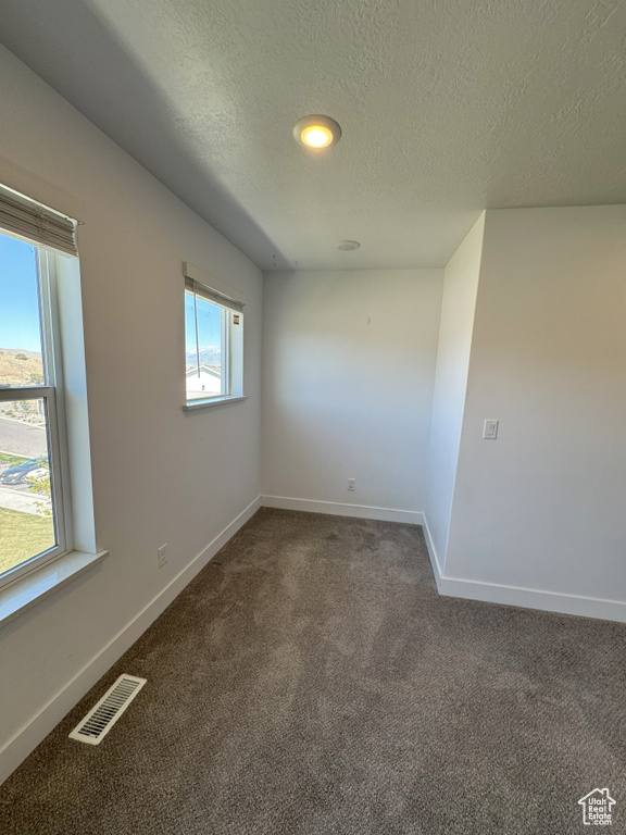 Spare room featuring a textured ceiling, baseboards, visible vents, and dark carpet