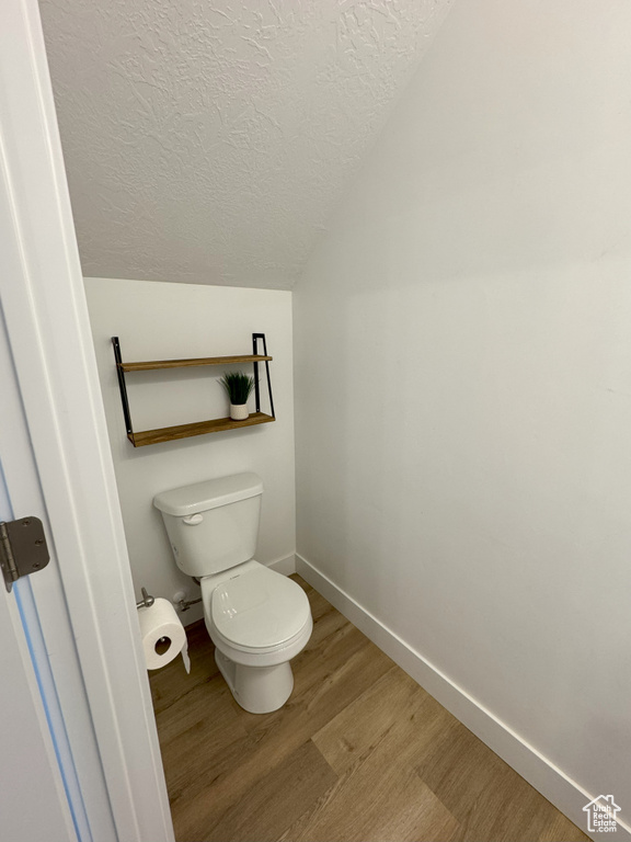 Bathroom with lofted ceiling, toilet, wood finished floors, a textured ceiling, and baseboards