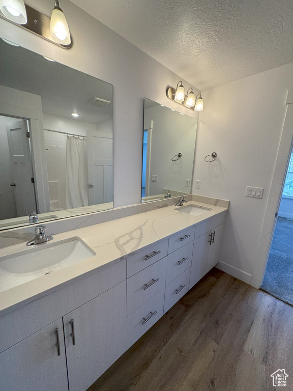Full bathroom featuring a sink, double vanity, a textured ceiling, and wood finished floors