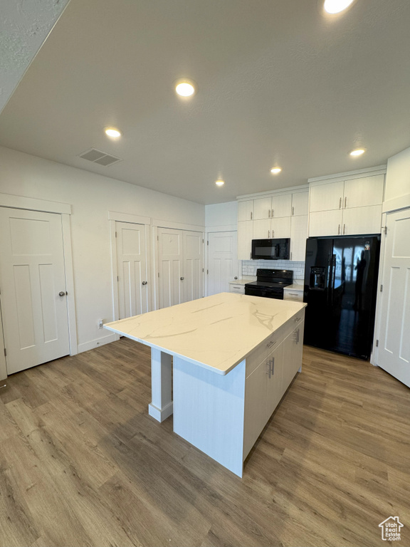 Kitchen with wood finished floors, black appliances, visible vents, white cabinets, and a kitchen island