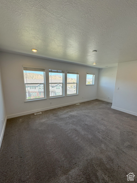 Unfurnished room featuring baseboards, dark colored carpet, visible vents, and a textured ceiling