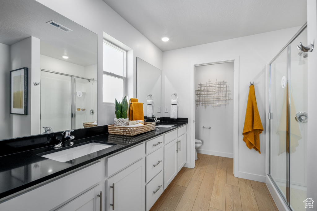 Bathroom featuring a sink, hardwood / wood-style floors, visible vents, baseboards, and a shower stall