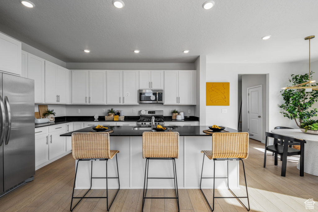 Kitchen featuring dark countertops, white cabinets, appliances with stainless steel finishes, and a kitchen bar