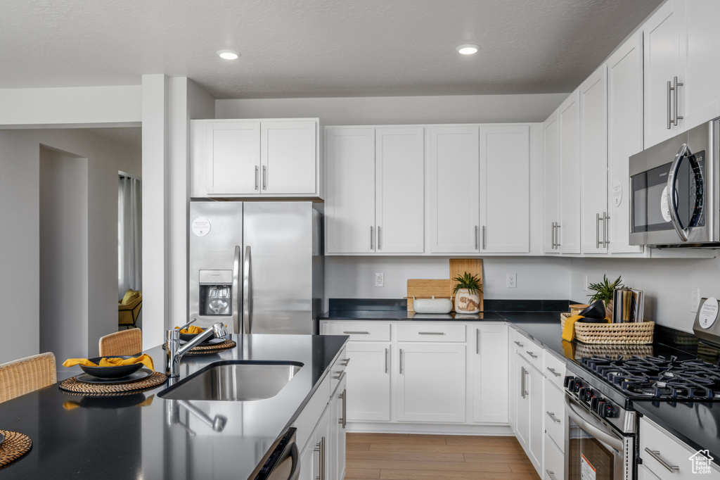 Kitchen featuring a sink, dark countertops, stainless steel appliances, light wood-type flooring, and recessed lighting