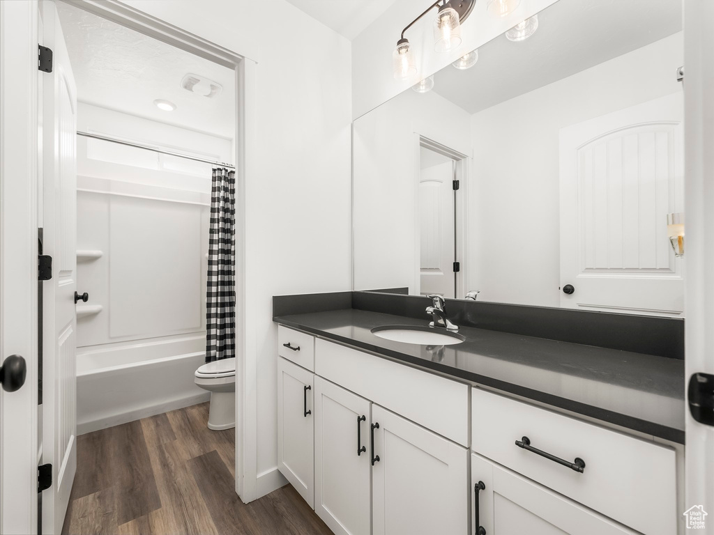 Bathroom with vanity, toilet, shower / bathtub combination with curtain, and wood finished floors