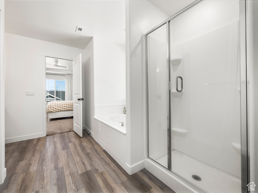 Bathroom featuring wood finished floors, a bath, ensuite bathroom, baseboards, and a shower stall