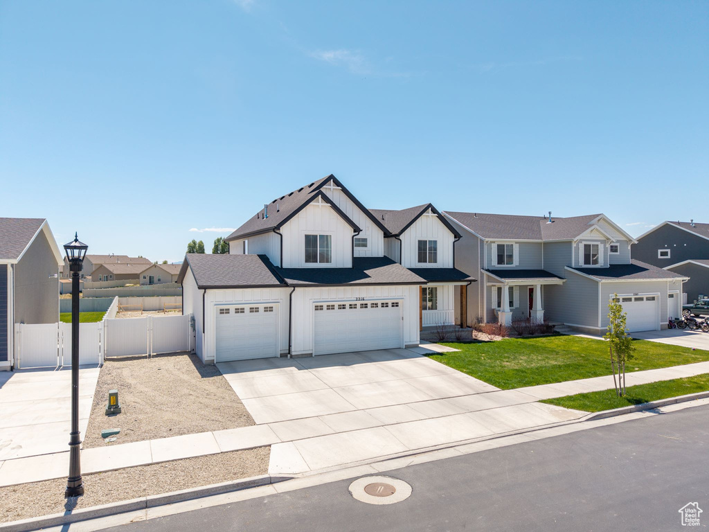 View of front facade featuring fence, a residential view, concrete driveway, a front lawn, and board and batten siding