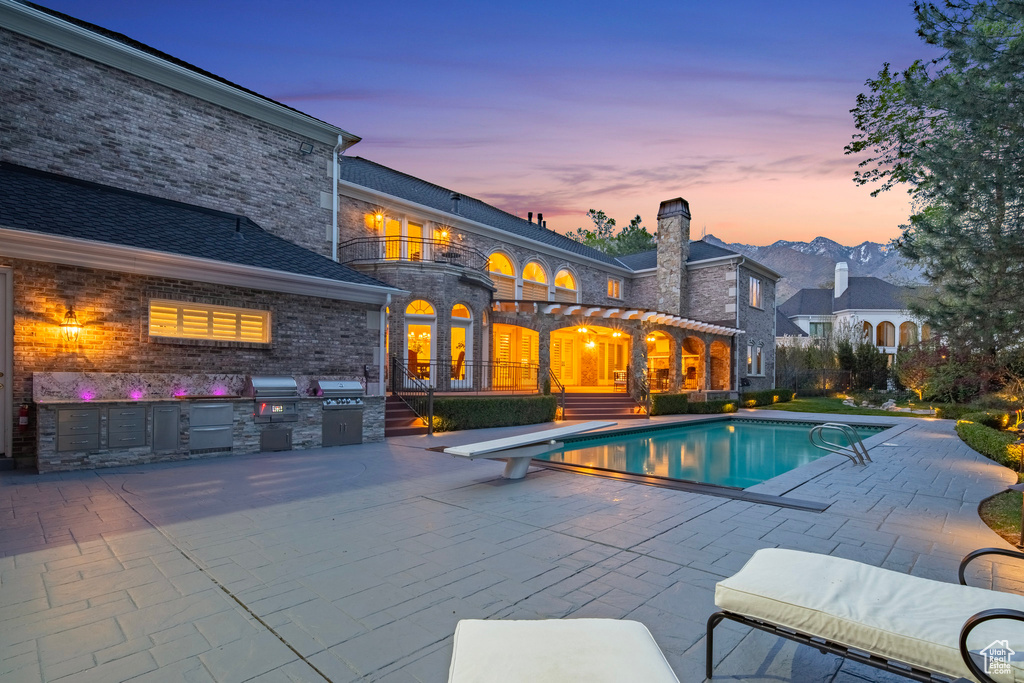 Outdoor pool with a diving board, grilling area, an outdoor kitchen, and a patio