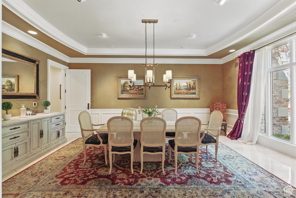 Dining space featuring crown molding, a chandelier, a decorative wall, and wainscoting
