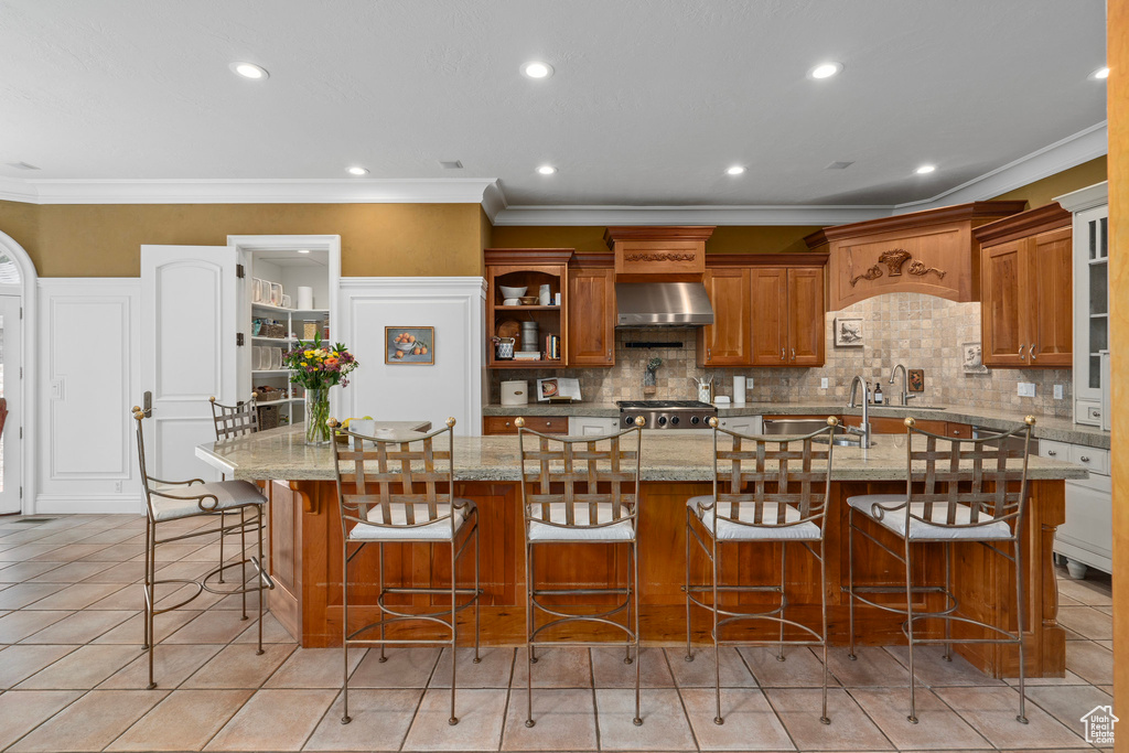 Kitchen with ornamental molding, a sink, brown cabinets, wall chimney range hood, and tasteful backsplash