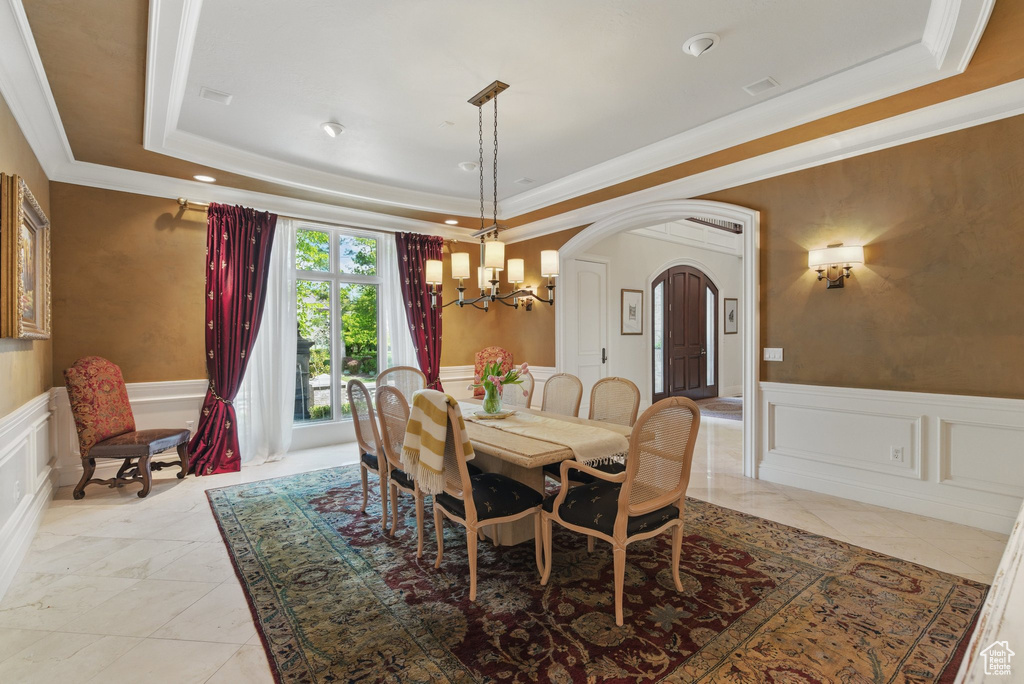 Dining room featuring a tray ceiling, an inviting chandelier, wainscoting, a decorative wall, and arched walkways