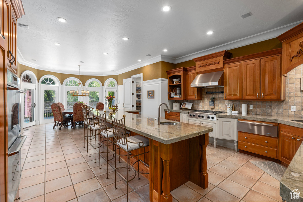 Kitchen featuring a sink, wall chimney exhaust hood, crown molding, a warming drawer, and light tile patterned flooring