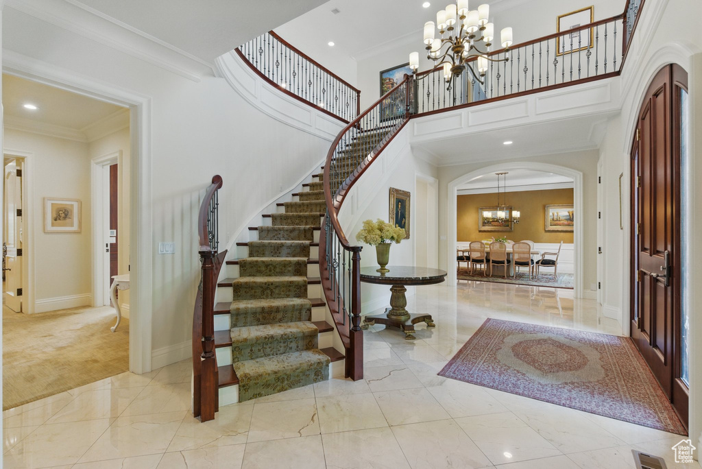Entrance foyer featuring an inviting chandelier, crown molding, a towering ceiling, arched walkways, and stairs