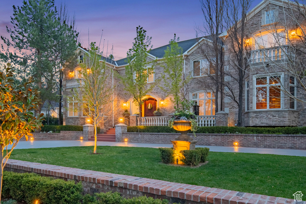 View of front of house featuring stone siding, a front yard, brick siding, and a balcony