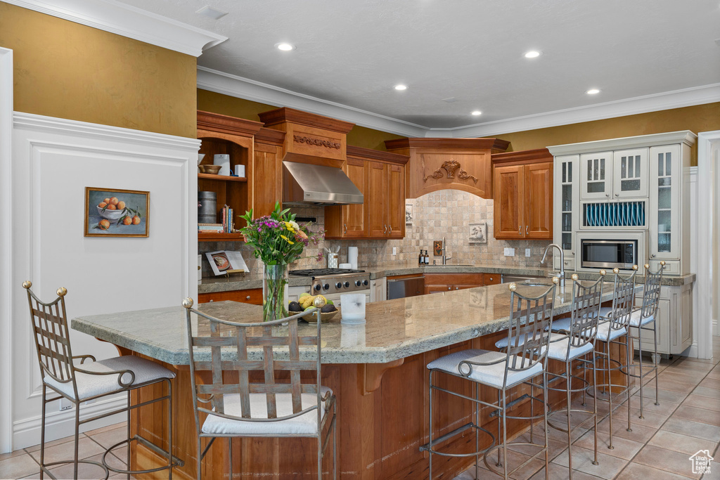 Kitchen featuring light tile patterned floors, a sink, wall chimney exhaust hood, brown cabinets, and appliances with stainless steel finishes