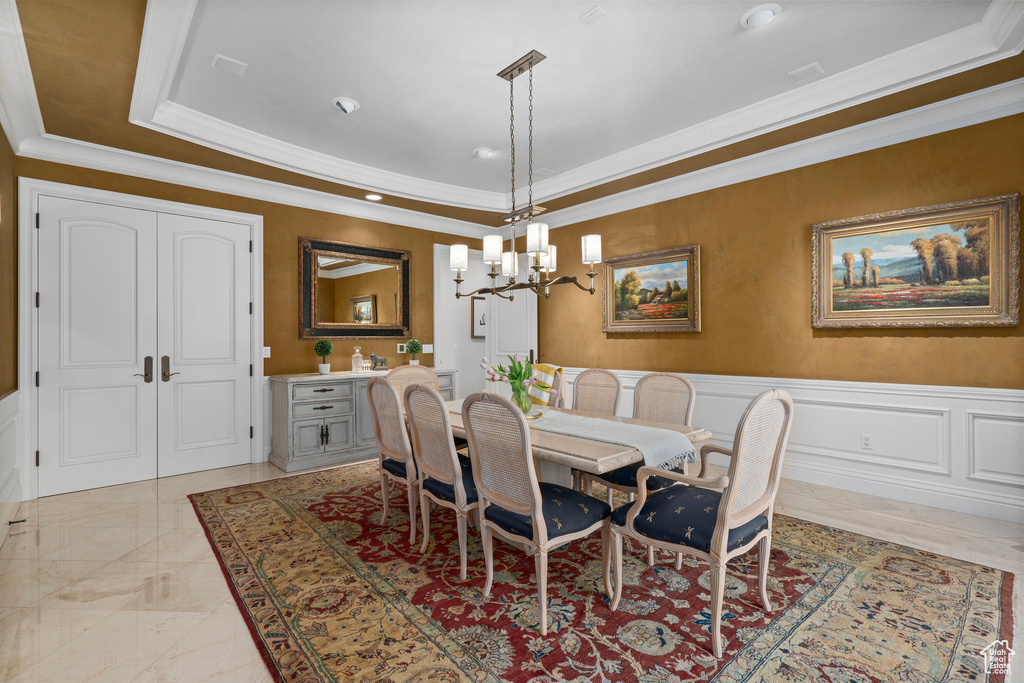 Dining area featuring an inviting chandelier, wainscoting, a raised ceiling, and ornamental molding