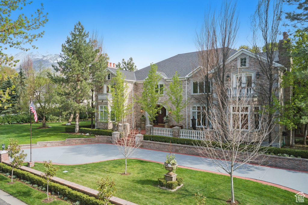 View of front of property with a chimney, a balcony, a front lawn, and stone siding