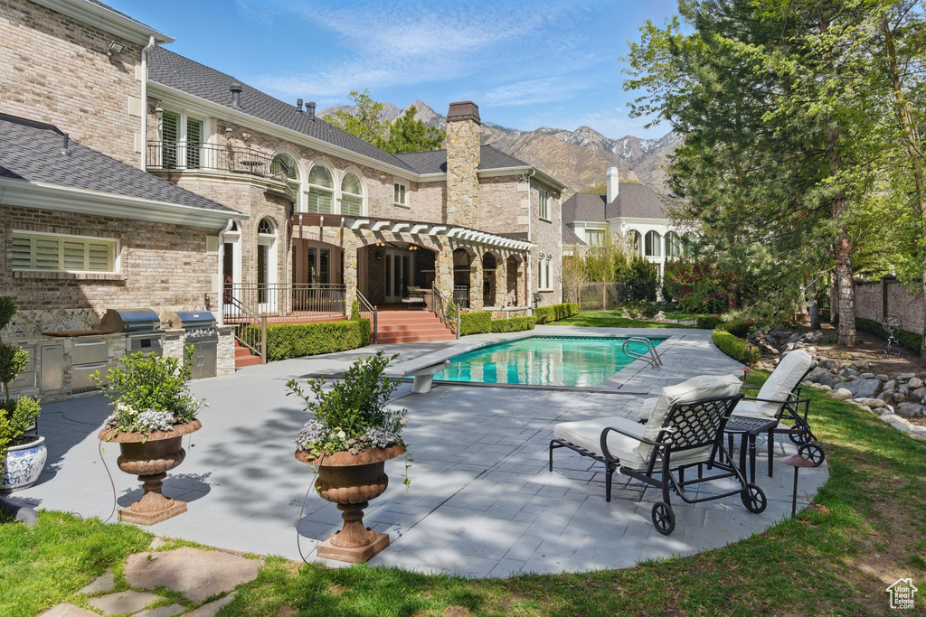 Outdoor pool featuring an outdoor kitchen, a diving board, a mountain view, a grill, and a patio area