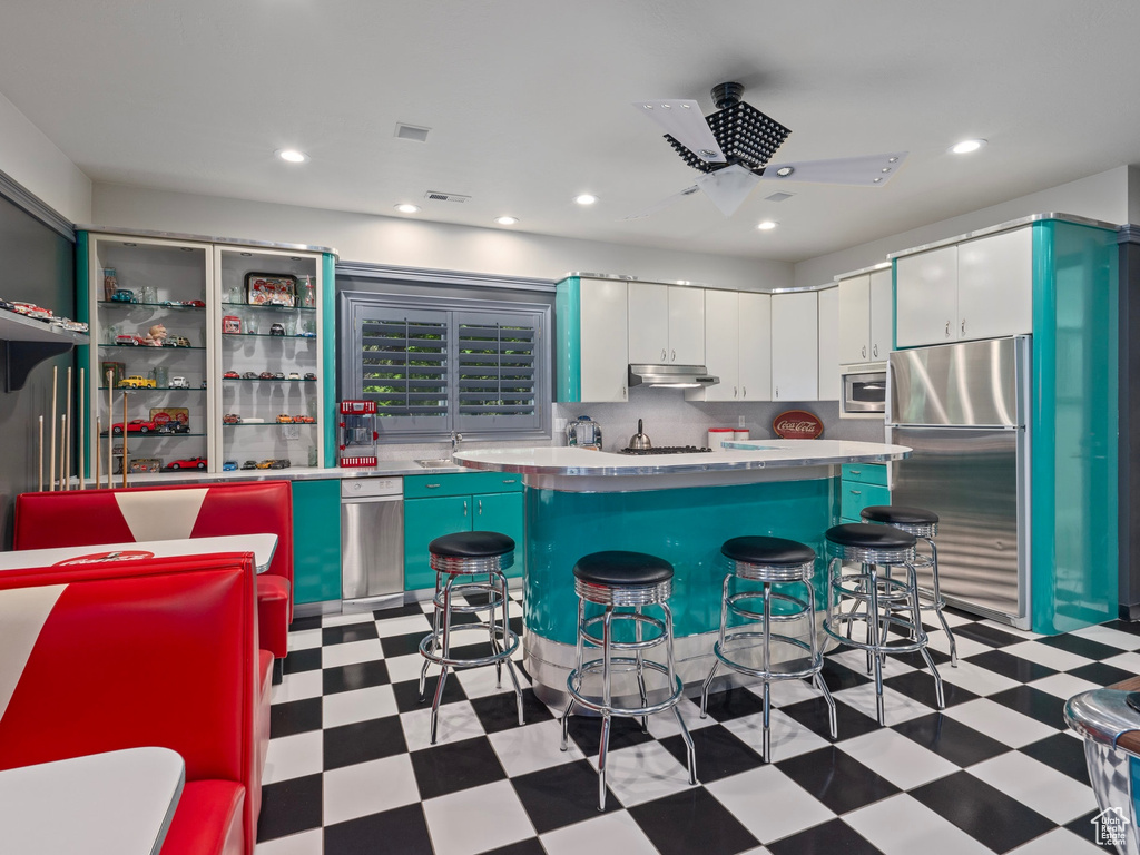 Kitchen featuring a breakfast bar, light floors, under cabinet range hood, ceiling fan, and appliances with stainless steel finishes