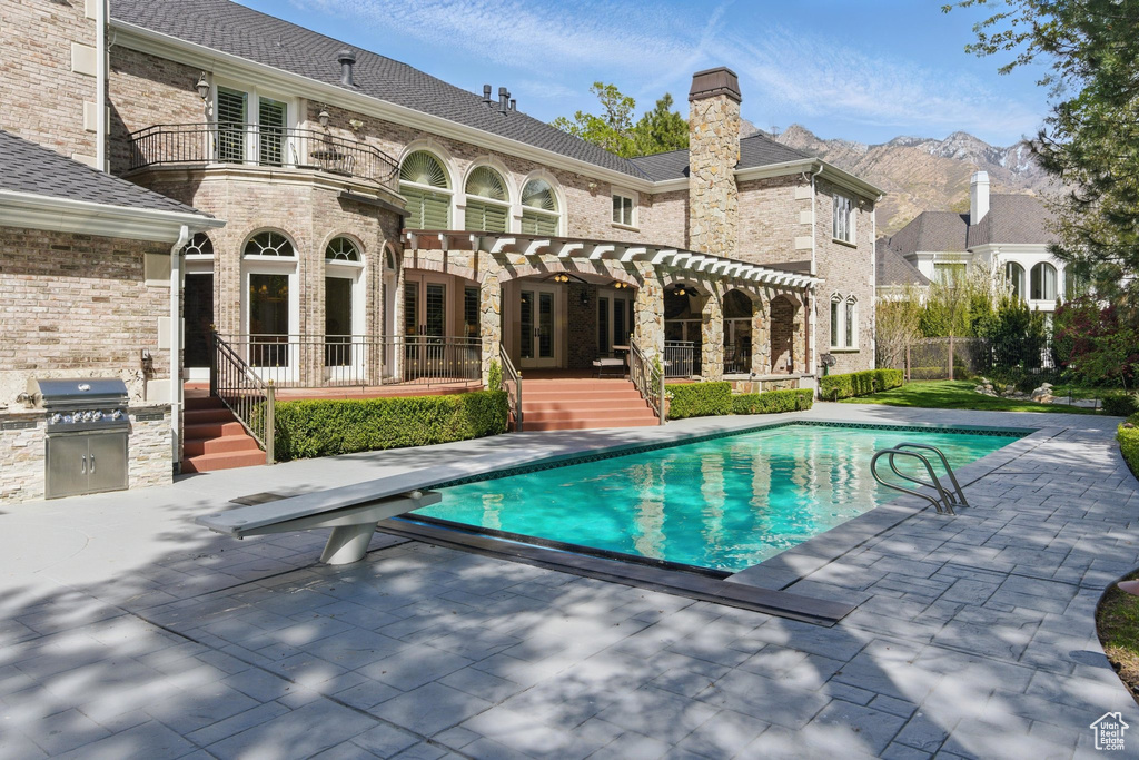 Back of property with a balcony, a chimney, french doors, a patio, and an outdoor pool