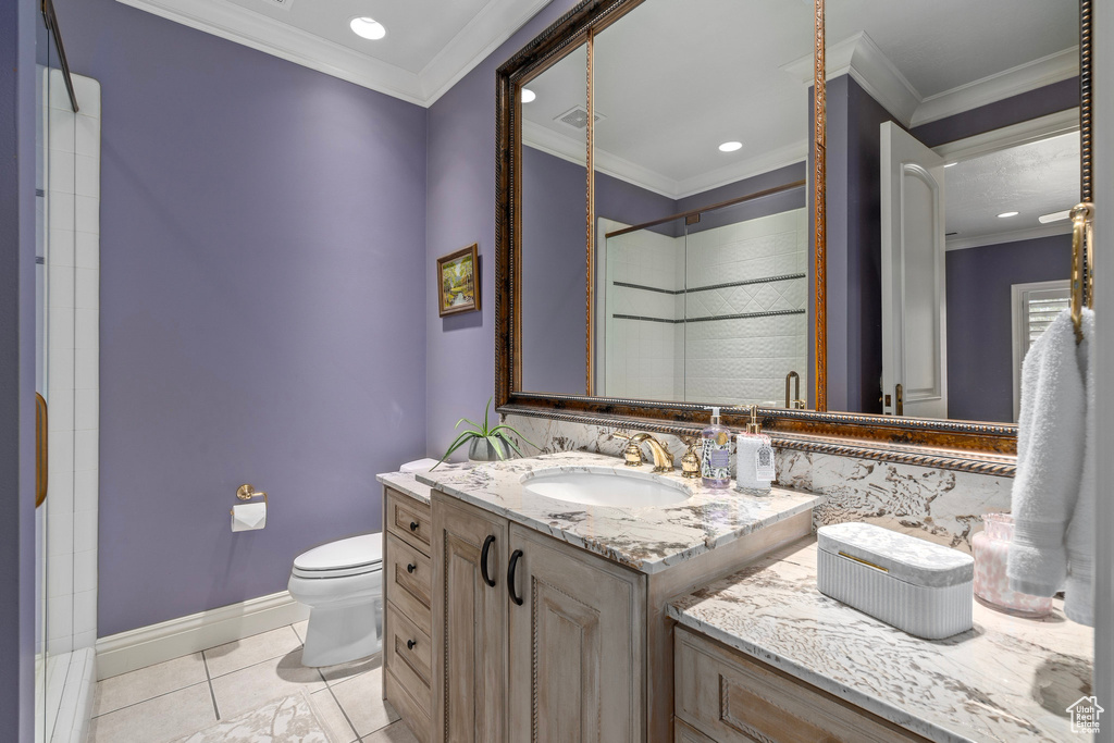 Bathroom featuring toilet, vanity, tile patterned floors, crown molding, and tiled shower