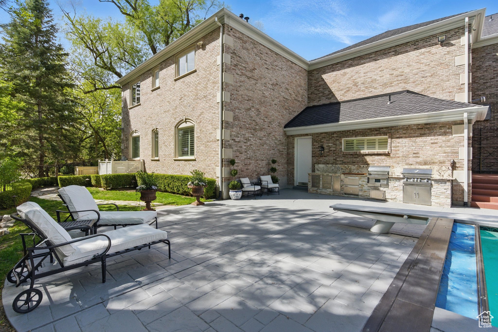 Rear view of house with a patio, an outdoor kitchen, brick siding, and a pool