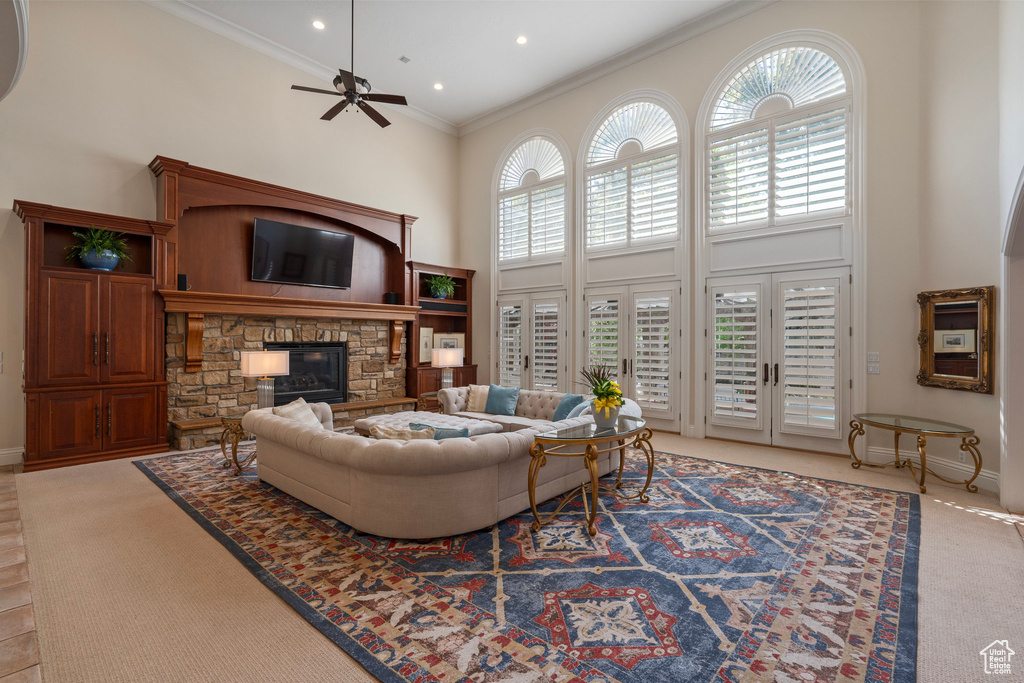 Living room with light colored carpet, a towering ceiling, ornamental molding, ceiling fan, and a stone fireplace