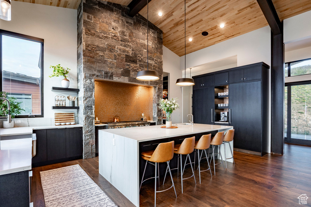 Kitchen featuring open shelves, high vaulted ceiling, wooden ceiling, a kitchen bar, and light countertops