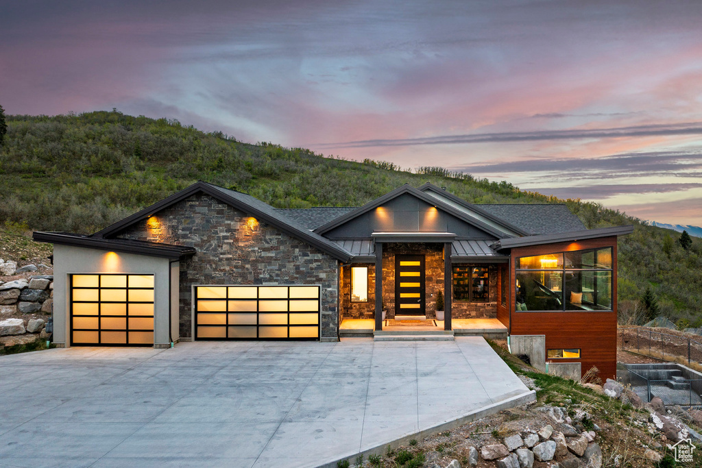 Contemporary house with a standing seam roof, metal roof, an attached garage, concrete driveway, and stone siding