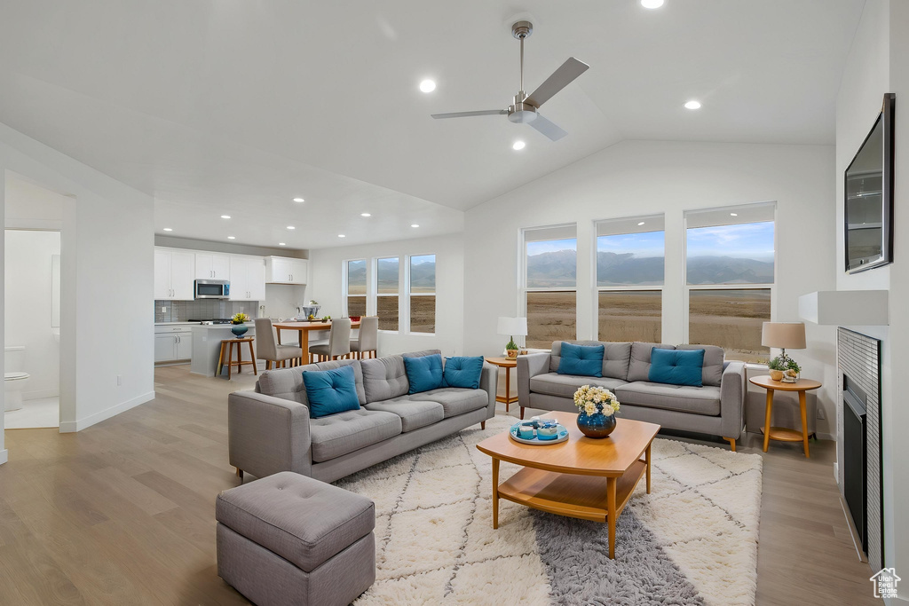 Living area with light wood-style flooring, lofted ceiling, a ceiling fan, recessed lighting, and a fireplace