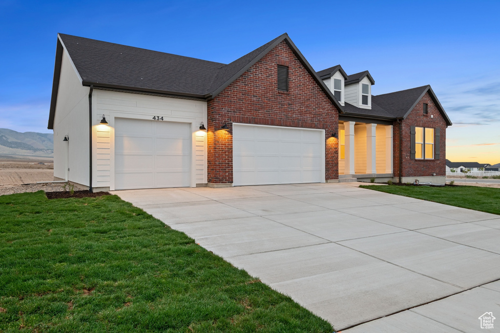 View of front of house featuring an attached garage, a shingled roof, a front lawn, brick siding, and driveway
