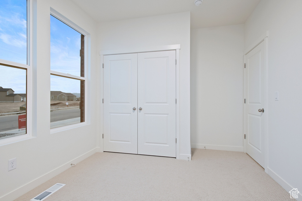 Unfurnished bedroom with light colored carpet, a closet, visible vents, and baseboards