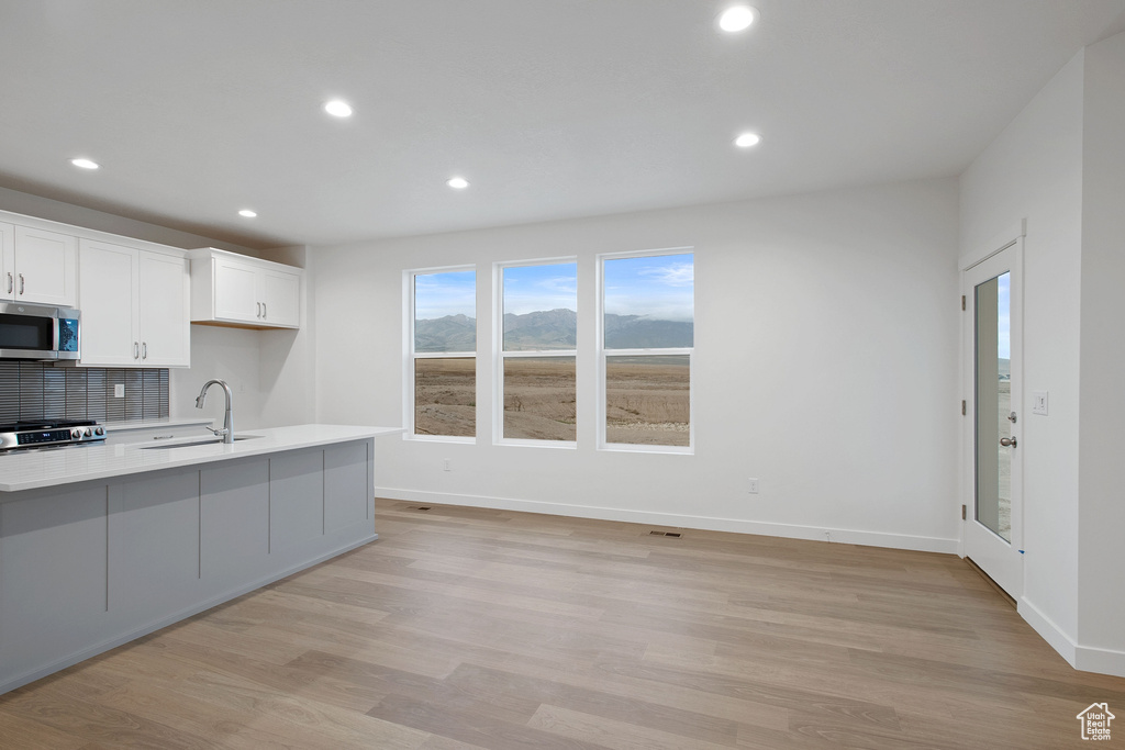 Kitchen featuring a sink, white cabinets, stainless steel microwave, light countertops, and tasteful backsplash