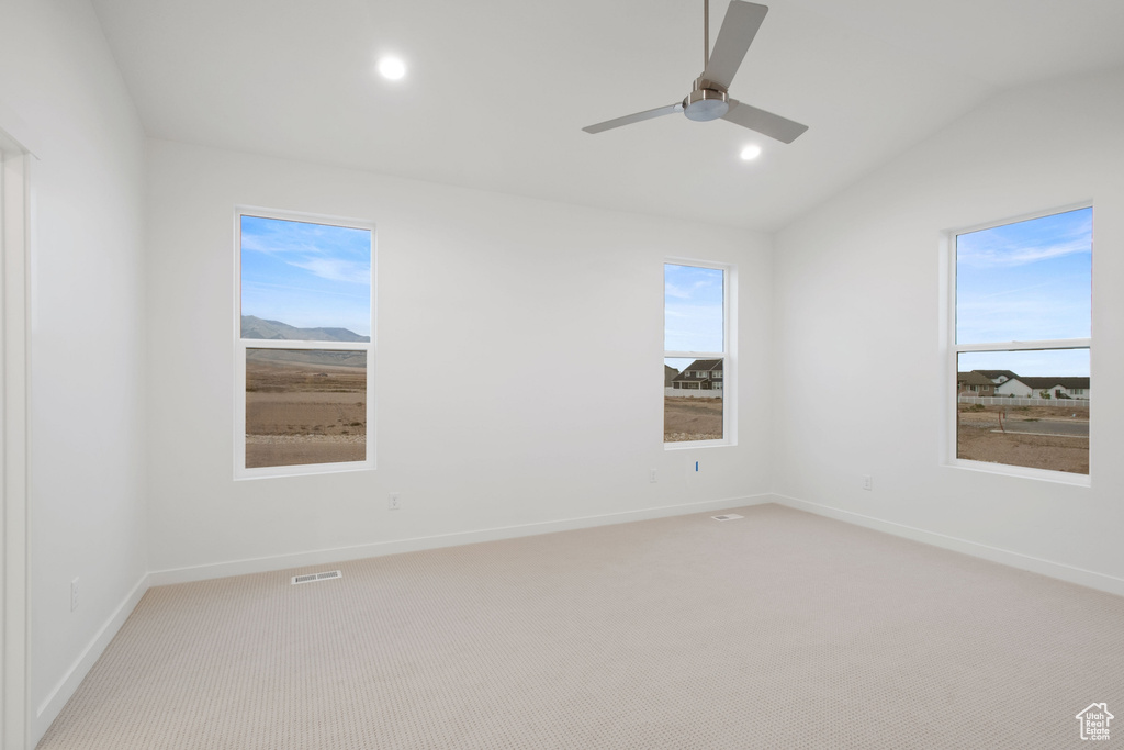 Spare room with a ceiling fan, visible vents, baseboards, light colored carpet, and vaulted ceiling