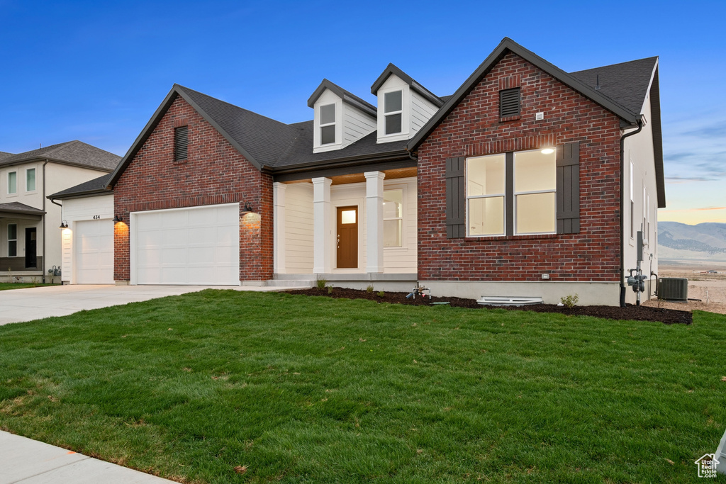 Cape cod-style house featuring a garage, central air condition unit, concrete driveway, a front lawn, and brick siding