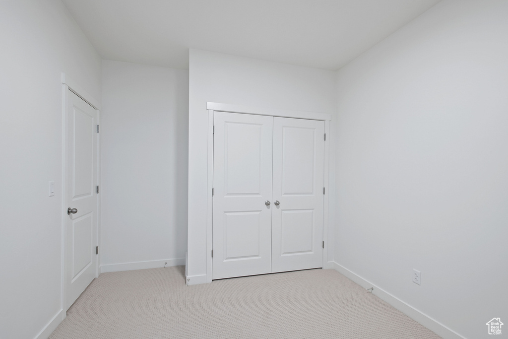 Unfurnished bedroom featuring light colored carpet, a closet, and baseboards